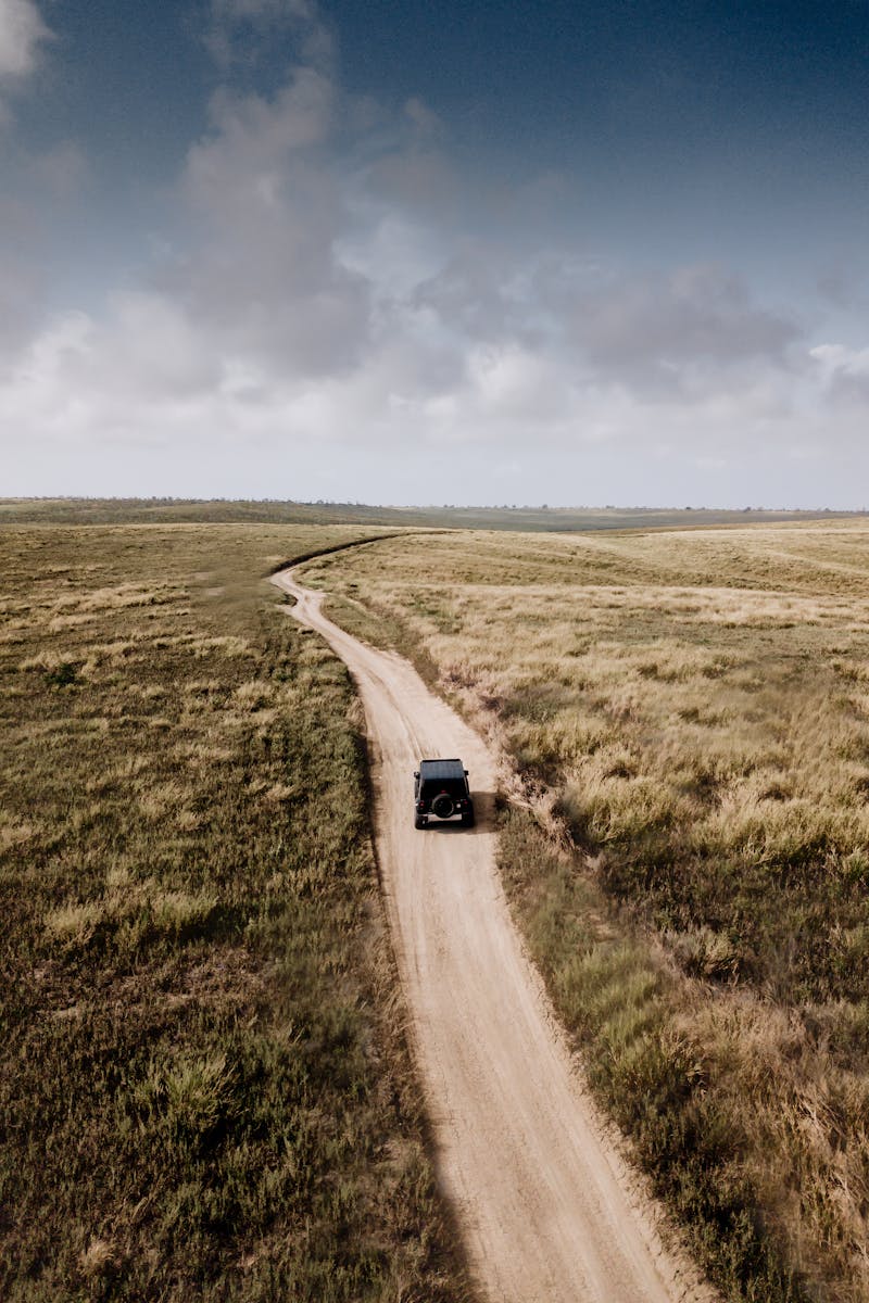 A vehicle travels on a winding dirt road through rural Caboledo, Angola.